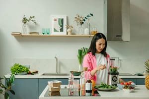 Woman preparing a healthy smoothie with fresh fruits and spinach in a modern kitchen for clean eating recipes.