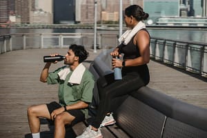 Healthy Habits – outdoor workout break with two people hydrating after exercise on a riverside boardwalk
